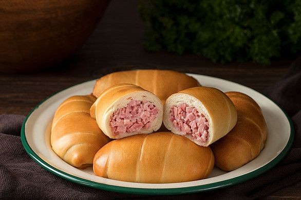 Plate of golden brown baked rolls filled with pink minced meat filling.